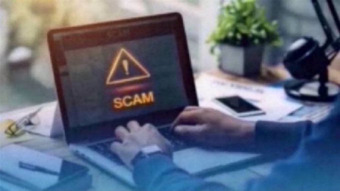 A stock photo showing hands typing on a laptop displaying a red warning triangle with 'SCAM' text on the screen.