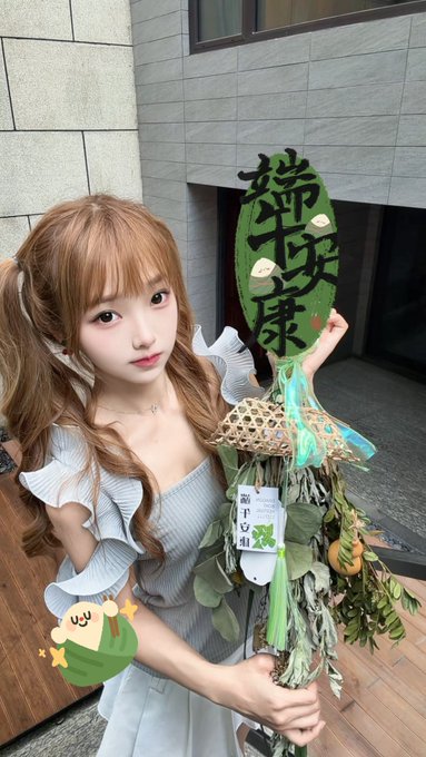 The image features a young woman with long brown hair, dressed in a white dress, holding an umbrella that has Chinese characters written on it. She appears to be posing for a photo or participating in an event related to Chinese culture. The background of the image is blurred and does not provide enough information about the context behind the scene.