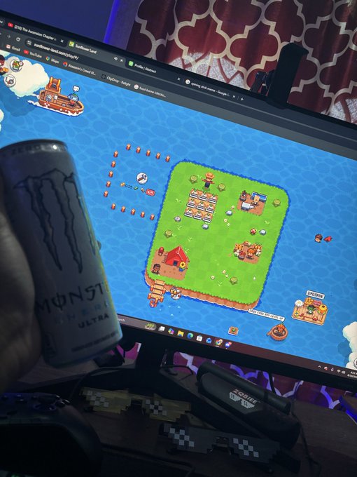 A hand holds a white Monster Energy Ultra can in front of a monitor displaying Sunflower Land gameplay, a blockchain farming game by 0xSunflowerLand. Visible text on screen includes the browser tabs, Discord, Gmail, YouTube, and OpenSea icons, with a taskbar at the bottom showing various applications open.