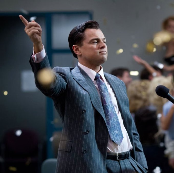 Leonardo DiCaprio, in a pinstripe suit, points defiantly with his arm raised as gold confetti rains down around him. The image captures the celebratory "Wolf of Wall Street" scene, which mirrors the post's celebration of crypto's unique potential for early "0→1" equity opportunities that traditional industries like AI rarely offer.