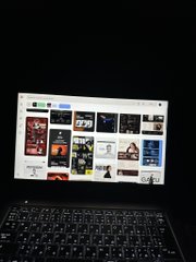 A dark photograph of a laptop screen displaying a grid of images, with the keyboard faintly visible below.