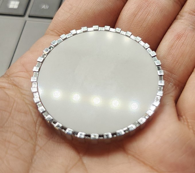 A close-up of a hand holding a round white cabochon stone or pendant surrounded by a silver rhinestone border.