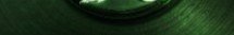 A close-up, low-light shot of a green textured surface, possibly fabric or canvas, with a circular object partially visible at the top.