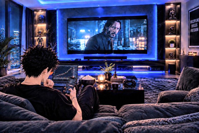 A person relaxing on a gray beanbag chair in a dimly lit, blue-LED-lit living room, watching Keanu Reeves as John Wick on a large TV while holding a smartphone, with a laptop showing a chart nearby.