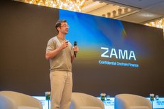 A man speaks at a podium during a presentation, with a large screen behind him displaying the "ZAMA" logo and the tagline "Confidential Blockchains."