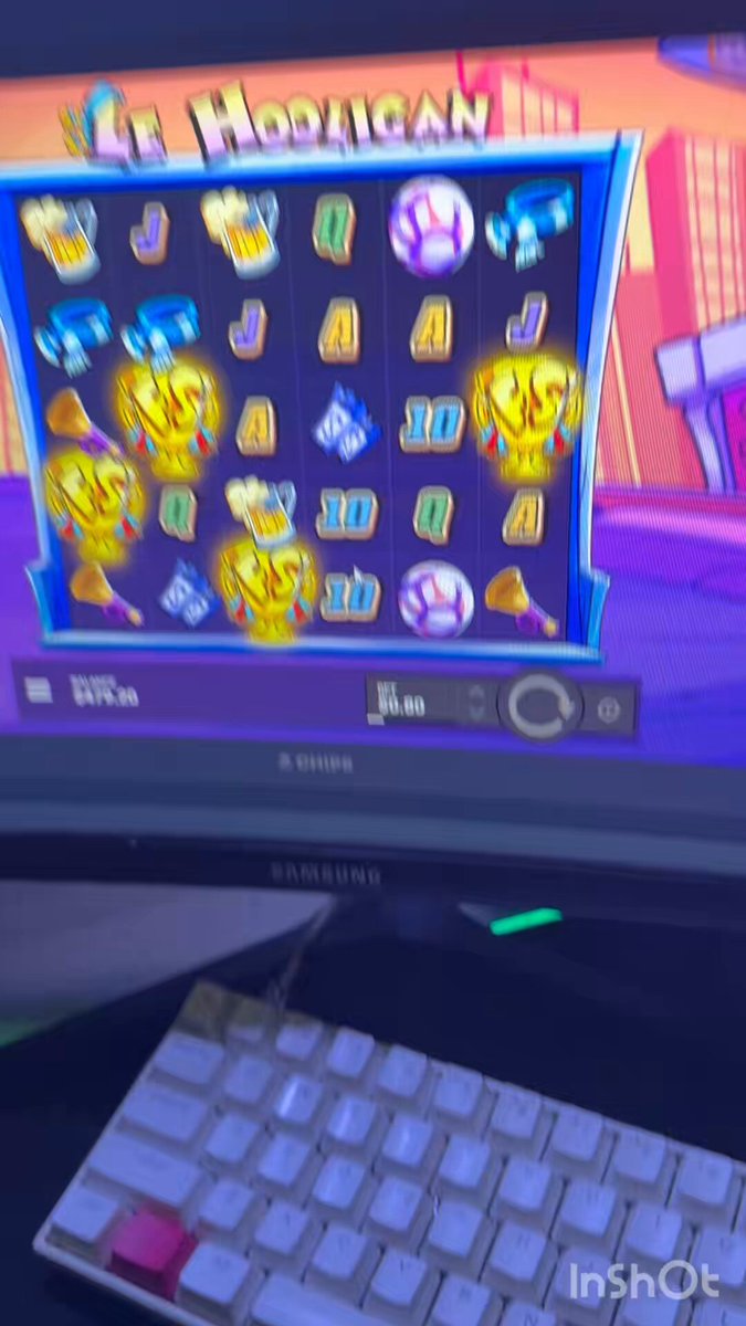 The image shows a computer monitor displaying a slot machine game, with various symbols such as a cat, a dog, and a number 10 visible on the screen. The monitor also has a keyboard nearby, suggesting that someone might be playing the slot machine while working or studying at their desk.