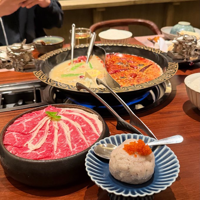 A hot pot feast featuring a split yin-yang broth with spicy red and creamy white sides, accompanied by beautifully marbled raw beef slices and a taro ball topped with orange roe, perfect for a "gmonad happy weekend!" celebration.