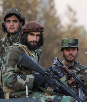 The image shows three armed individuals in camouflage, likely Taliban fighters, reflecting the governing body that has banned Bitcoin and crypto trading in Afghanistan. This ban comes with threats of prosecution for traders and businesses, with at least 13 crypto shops closed.