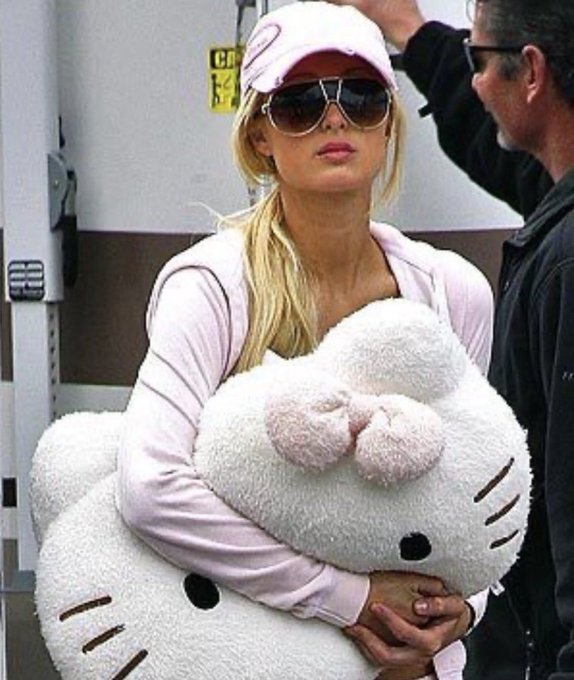 Britney Spears wearing a pink cap and sunglasses, carrying a large white Hello Kitty plush pillow.
