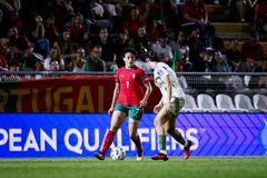 A Portugal vs. Mexico soccer match from the European Qualifiers, with a player in a red Portugal kit defending against a player in a white Mexico kit.