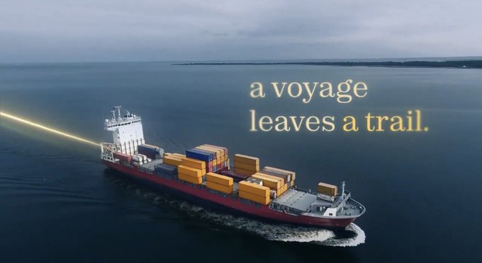 An aerial shot of a cargo ship loaded with containers sailing on calm blue water, overlaid with the text 'a voyage leaves a trail.'