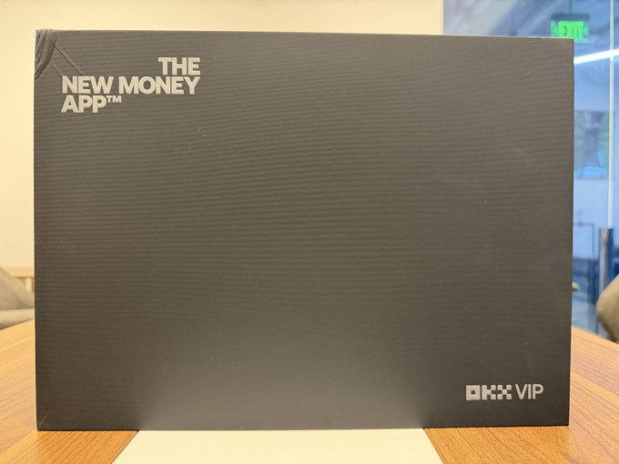 A black box labeled 'THE NEW MONEY APP' and 'OKX VIP' sitting on a wooden surface.