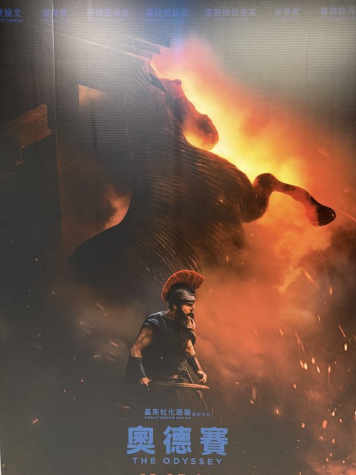 A movie poster for 'THE ODYSSEY' (奥德賽) featuring a warrior with a plumed helmet standing beneath a massive flaming bull, with Chinese text credits along the top including names like 麦斯·米科尔森, 莎莲·希, 罗伯特·派迪森, and 余塔克.