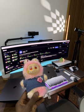 A hand holds a pink Labubu plush toy in front of a dual-monitor trading setup displaying cryptocurrency charts, visually representing the "Labubu" token mentioned in the post that turned a profit of $20K.