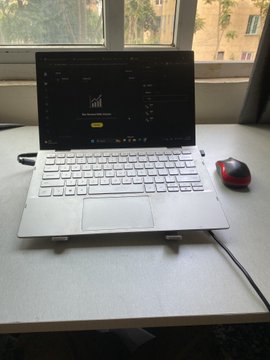 The image shows a laptop computer sitting on top of a desk, with a mouse next to it. There are two windows visible in the background - one is a window on the left side of the frame, while the other is a window on the right side. The laptop appears to be set up for use, possibly for work or study purposes.