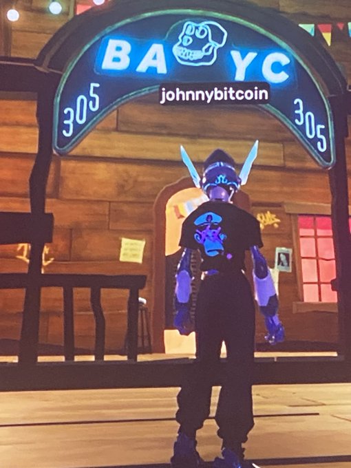 A 3D animated character stands with their back to the viewer under a neon sign reading "BAYC" and "305" with a "johnnybitcoin" label overlay, set in a wooden interior.
