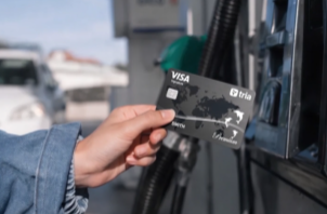 A person's hand is seen inserting or removing a black Visa credit card from what appears to be an ATM or card reader, with a blurred outdoor background.