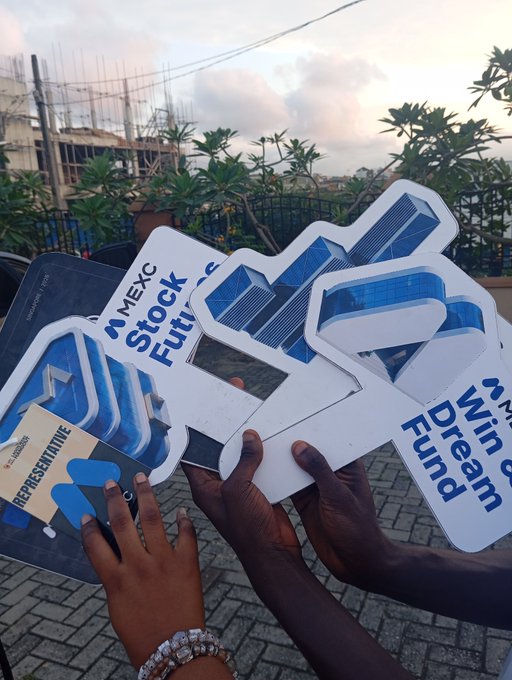 People holding blue and white cutout signs featuring 'MEXC', 'Stock', 'Futures', and 'Dream Fund' logos at what appears to be a brand event.