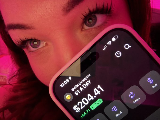 A close-up of a person's face lit in pink, partially obscured by a smartphone displaying a crypto trading app with a price of '$204.41' and a profit of '+$4.71'.