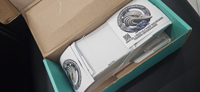 An opened cardboard shipping box lined with stacked white envelopes or mailers bearing circular logos and QR codes.