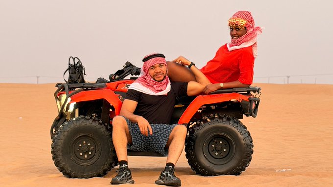 A couple enjoys a desert ATV ride, with the man's attire and the woman's headdress suggesting a Middle Eastern setting, likely celebrating successful trades in $BANK, $AKE, and $BTW.