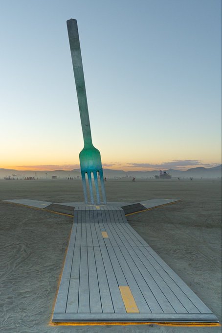 A giant glowing fork sculpture stands in a desert at sunset, with a wooden walkway leading to it, symbolizing the "$FORK" token highlighted as the first trending item in the accompanying post.