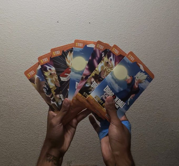 A pair of hands fanning out several Dragon Ball trading cards, each labeled 'ST01'.