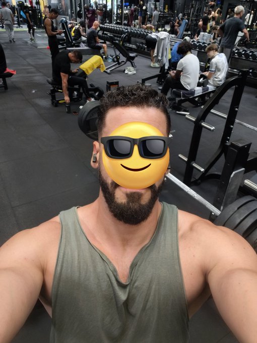 A man takes a gym selfie in an olive green tank top, with a sunglasses emoji covering his face, while other gym-goers work out on benches and equipment in the busy weight room behind him. The image serves as "proof of workout" to engage followers and encourage them to share their own gym photos in exchange for a follow.