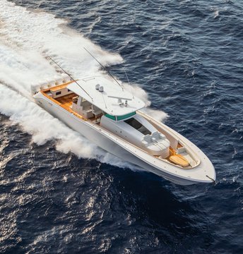 An aerial view of a luxurious white and wood-trimmed yacht speeding across deep blue ocean waters.