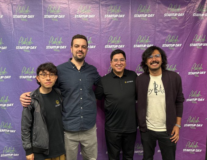 A photo of four men posing in front of a purple 'Phuket Startup Day' event backdrop, with two wearing black shirts with an 'ACRIO' logo.