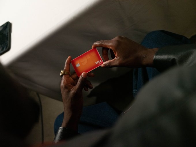 A close-up of a person's hands holding a red VISA debit card, wearing a gold ring on one finger.