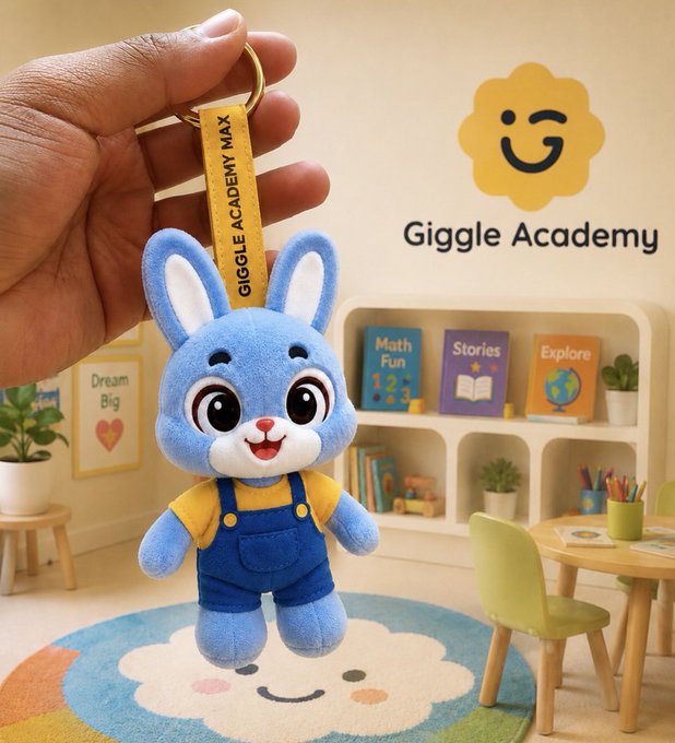 A hand holding a 'GIGGLE ACADEMY MAX' plush keychain of a blue cartoon bunny in yellow shirt and blue overalls, displayed in a colorful children's room setting with the Giggle Academy logo.