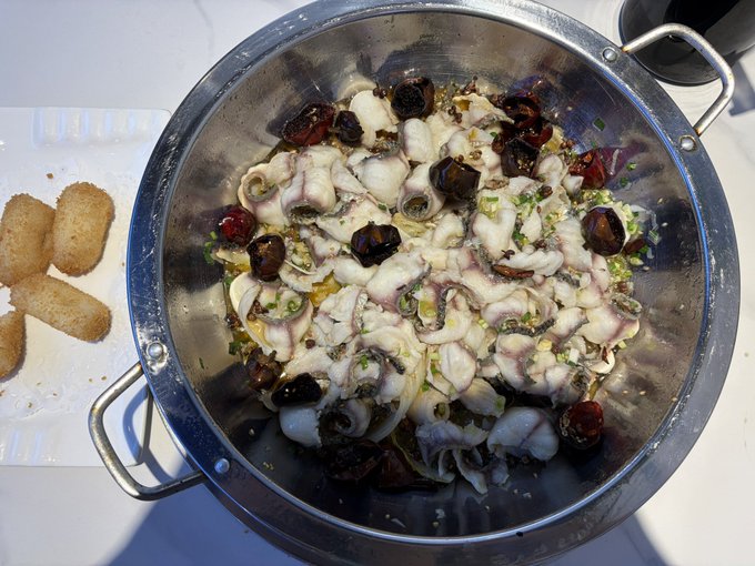 A stainless steel colander filled with fresh seafood—octopus, whelks, and shellfish—rests beside pieces of toasted bread, suggesting a casual meal being prepared. The image reflects the post's sentiment of stepping away from the fast-paced crypto world to savor simple, meaningful moments with family, embracing the present rather than chasing an uncertain future.