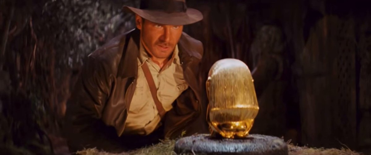 A man is holding a golden object near him while standing next to a tree at night. The image also shows that he has a key shaped like a squirrel in his hand. The context of the image suggests that someone has introduced a foreign currency, like Bitcoin or Ripple, into this man's pocket and possibly transferred its value directly into the linked wallet through a digital payment method. This could result in the golden item being converted to a monetary form.
