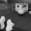 A black and white photo of a person wearing white sneakers, with one foot resting near a medicine ball labeled '30' and boxes in the background, suggesting a gym or workout setting.