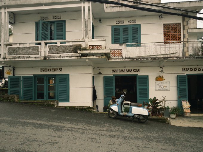 A vintage-style two-story building with teal shutters houses a business, with a light blue and white scooter parked in front.