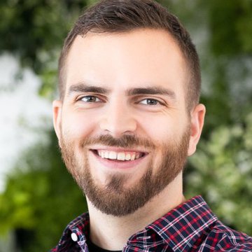 The image features a man with a beard wearing a plaid shirt, smiling at the camera. The background includes a green wall adorned with white flowers. There are also some text elements in the image that seem unrelated to the main subject of the photo.