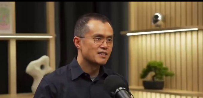 A man with glasses and a dark shirt speaks into a microphone in what appears to be a podcast or interview setting, with a bonsai tree and security camera visible in the background. The image likely depicts CZ (Changpeng Zhao), the Binance founder, as he discusses the early conviction and personal sacrifice—including selling his apartment—that led to his Bitcoin accumulation before founding the exchange.
