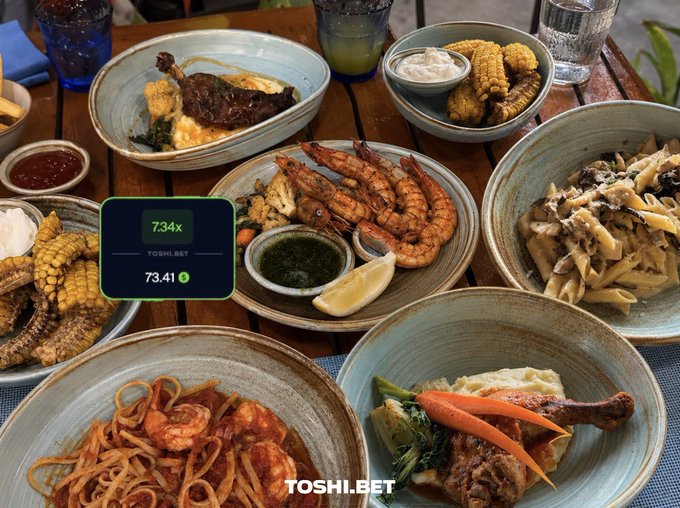 The image shows a table filled with various dishes of food, including pasta, shrimp, corn, and other entrees. The table also has several cups and bowls containing different types of sauces and condiments. A green screen displays a message that reads "free lunch today thanks to @ToshiBet smash or pass?". This suggests that the image is related to a social media post promoting a meal deal at a restaurant, where users can enjoy a free lunch by sharing their photo with the hashtag #toshibetbet.