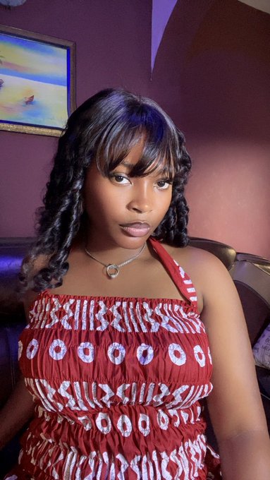 A young woman with long curly hair poses indoors, wearing a red patterned off-shoulder top and a circular pendant necklace, with a painting visible on the wall behind her. The image accompanies a personal introduction from an 88-year-old marketing creative seeking connections with artists, collectors, and others in the NFT and crypto space.