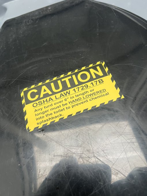 A yellow caution sticker on a scratched surface reads "CAUTION OSHA LAW 1729.17B Any turd over 6" in length or longer must be HAND LOWERED into the toilet to prevent chemical splashback," humorously playing into the post's joke about something found "in the shitter."