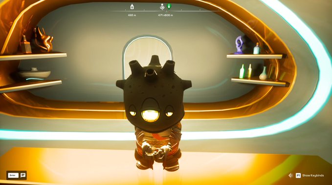 A video game screenshot showing a small character in a black spiked helmet with a glowing yellow visor standing in a futuristic room with curved yellow walls and shelves displaying decorative items.