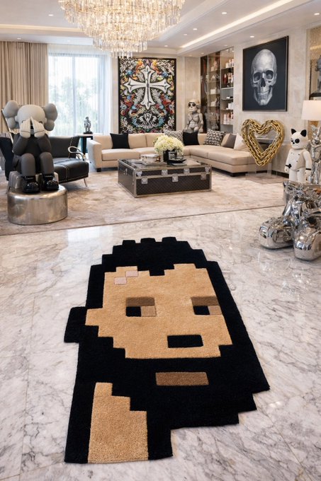 A luxurious living room interior featuring a large pixel-art style rug depicting a cat face, surrounded by designer furniture including a KAWS sculpture, crystal chandelier, and skull artwork.