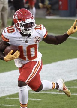 An NFL football player wearing a white Kansas City Chiefs jersey with the number 10, running with the football on a field.