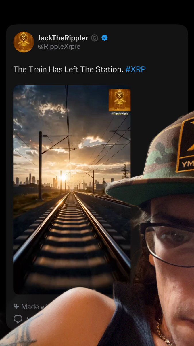 The image shows a man wearing glasses, a hat with an "Y" logo, and sunglasses taking a selfie at a train station. He has his arm outstretched towards the camera, capturing the moment. The background of the photo features a train track running through a cityscape under a cloudy sky. The caption on the post reads: "ALL ABOARD".