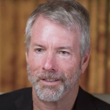 A headshot photograph of an older man with gray hair and a beard, smiling slightly against a warm blurred background.