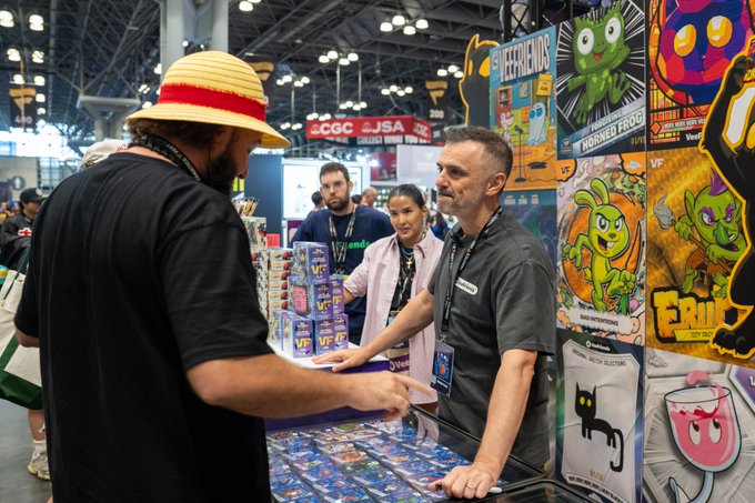 The caption should be informative and reflect the welcoming sentiment of the post.

**Caption:**
VeeFriends representatives engage with attendees at a busy convention booth, showcasing colorful character trading cards and plushies featuring recognizable NFT figures.