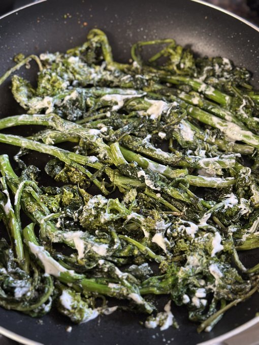 A close-up of sautéed dark leafy greens cooking in a black pan, drizzled with a creamy white sauce.