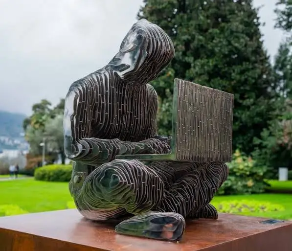 A dark, abstract seated sculpture with a hooded figure appears to interact with a rectangular panel, displayed outdoors on a wooden pedestal. The piece's contemplative, hunched form evokes the post's message of "Something sweet to throw away," suggesting a meditative reflection on discarding something once cherished.