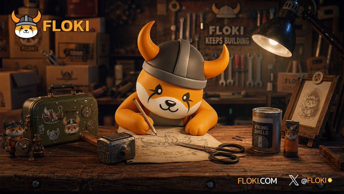 A promotional image for FLOKI cryptocurrency featuring the Viking-helmeted Shiba Inu mascot sitting at a workbench with drawing tools, a suitcase, and a can labeled 'VIKING SHIELD', along with 'FLOKI KEEPS BUILDING' text and social media handle '@FLOKI'.